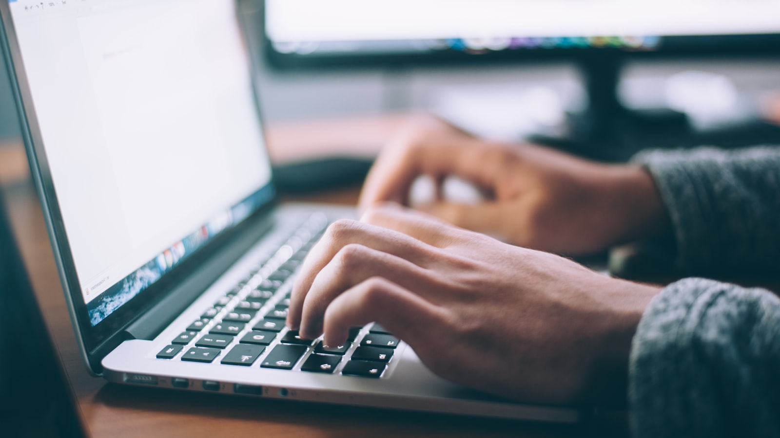 Hands typing on a laptop beside a second monitor